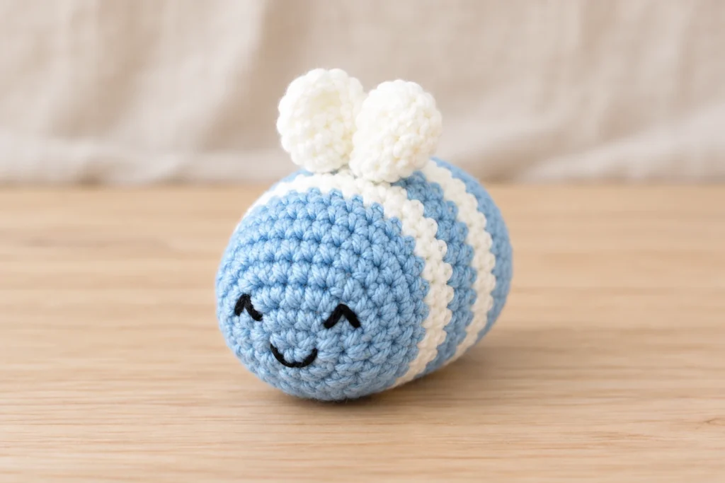 Crochet bee amigurumi pattern featuring a pastel blue and white striped bee with two white wings and an embroidered smile